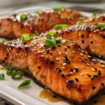['Juicy Air Fryer honey garlic salmon fillet garnished with parsley.', 'Close-up of skin-on salmon fillet drizzled with honey garlic sauce.', 'Side view of cooked salmon topped with minced garlic and parsley.', 'Delicious honey garlic salmon fillet in an air fryer setting.']
