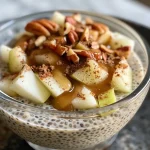 ['A close-up view of a creamy apple cinnamon chia pudding topped with chopped pecans.', 'Side angle of apple cinnamon chia pudding with diced apple and spices visible.', 'Textured chia pudding with apple chunks and a sprinkle of cinnamon in a glass cup.', 'Filled glass featuring layers of apple cinnamon chia pudding and pecan pieces.']