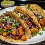 ['Close-up view of Butternut Squash Black Bean Tacos topped with cabbage and cilantro.', 'Side view of vibrant tacos filled with roasted butternut squash and black beans.', 'Colorful Butternut Squash Black Bean Tacos arranged on a plate with lime wedges.', 'Succulent tacos featuring butternut squash, black beans, and fresh toppings.']