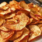 ['Close-up view of crispy cinnamon apple chips on a wooden surface.', 'Slices of cinnamon-dusted apple chips arranged neatly in a bowl.', 'A side view of golden-brown apple chips with a sprinkle of cinnamon.', 'Freshly made cinnamon apple chips showcased on a rustic plate.']