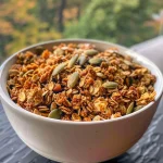 ['Close-up view of a bowl filled with healthy pumpkin spice granola featuring oats and pumpkin seeds.', 'Top-down perspective of a delicious serving of pumpkin spice granola with visible ingredients.', 'Side view of a colorful mix of granola, pumpkin seeds, and spices in a rustic bowl.', 'Detailed shot of granola showcasing pumpkin puree and spices blended together.']