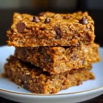 ['Close-up side view of a Protein Pumpkin Bar topped with dark chocolate chips.', 'A delicious Protein Pumpkin Bar, showcasing its moist texture and pumpkin flavor.', 'Side view of a Protein Pumpkin Bar with visible oats and chocolate chips.', 'Close-up image of golden-brown Protein Pumpkin Bars, highlighting their ingredients.']