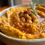 ['Close-up view of creamy pumpkin pie hummus in a bowl.', 'Side view of pumpkin pie hummus with a rustic background.', 'Thick pumpkin hummus garnished with spices and served in a dish.', 'Smooth pumpkin pie hummus displayed attractively on a wooden table.']