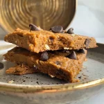 ['Close-up view of a Pumpkin Spice Protein Cookie with dark chocolate chips.', 'Side view of a freshly baked Pumpkin Spice Protein Cookie on a wooden surface.', 'A delicious Pumpkin Spice Protein Cookie highlighting its texture and chocolate chips.', 'Juicy Pumpkin Spice Protein Cookie with visible spices and chocolate chips.']