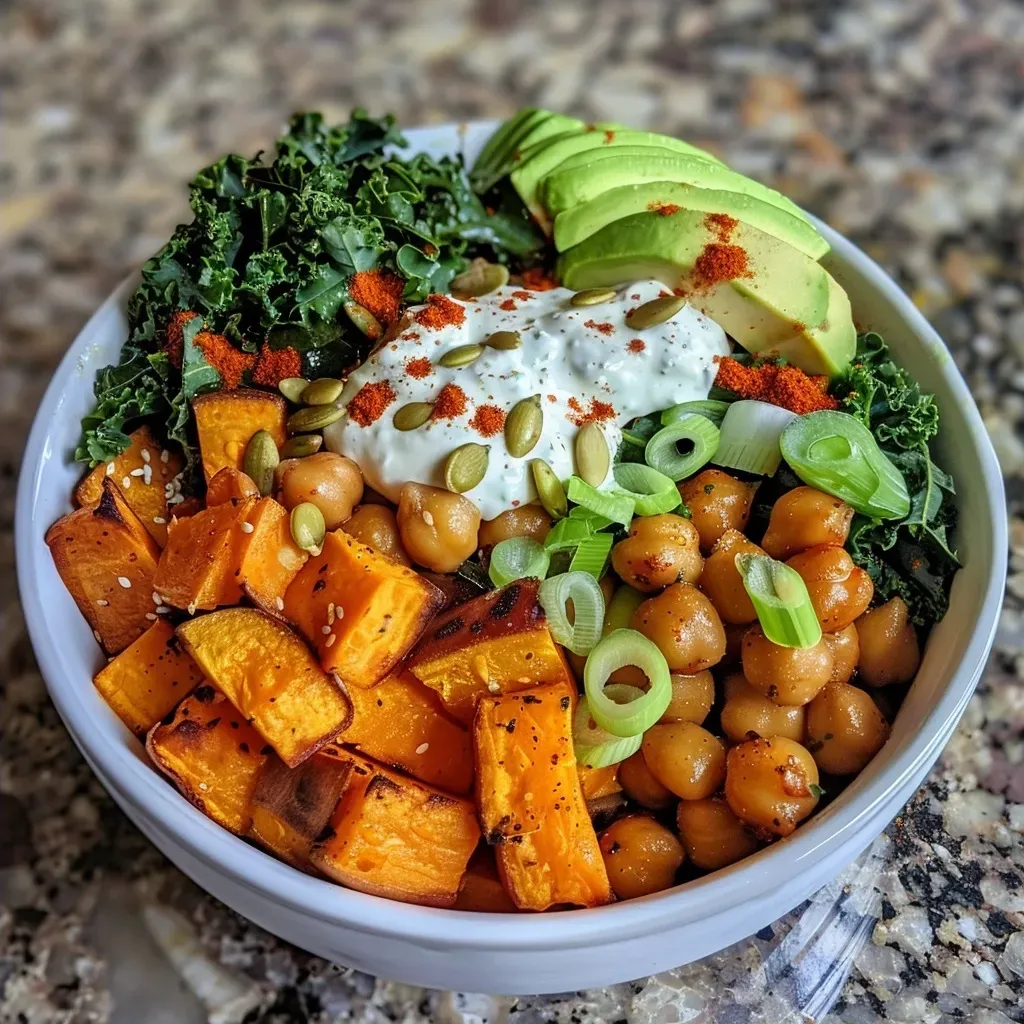 Close-up view of a roasted sweet potato bowl topped with crispy kale, pumpkin seeds, and yogurt dill sauce.