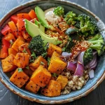 A vibrant Buddha bowl filled with roasted sweet potatoes, broccoli, red bell peppers, and zucchini.